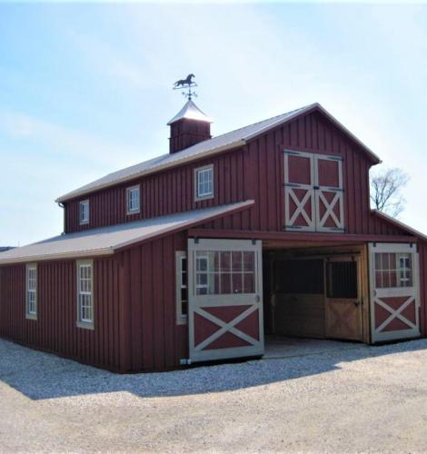 Red 2 story barn with white trim, windows, sliding doors, and a cupola with a horse weathervane.