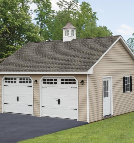 2 car garage with tan siding, two white garage doors, a side entry door, windows, and a brown shingle roof with a white cupola.
