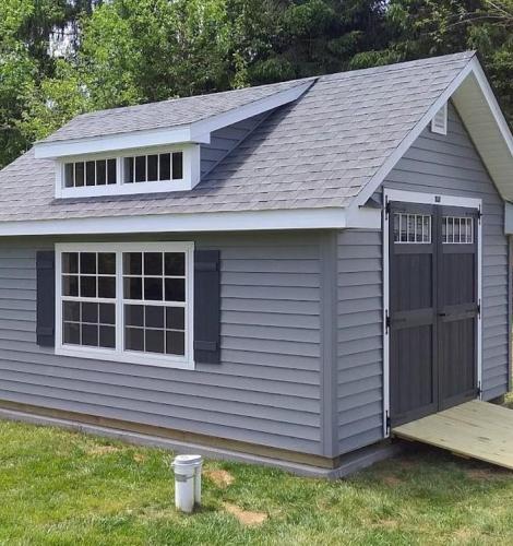 Deluxe Classic Cottage with gray siding, a light gray asphalt roof, windows with black shutters, and black double doors with a ramp.