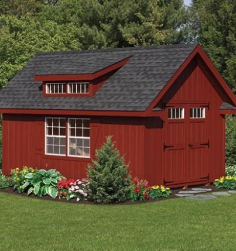 deluxe classic garden cottage with red siding, dormer, black roof, and shrubs along the perimeter
