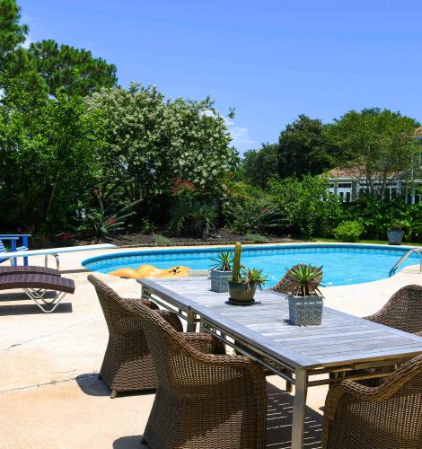 Backyard with a pool, lounge chairs, and an outdoor table with wicker chairs and small cacti plants.