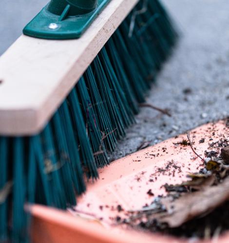 Broom pushing dirt and leaves into dustpan.