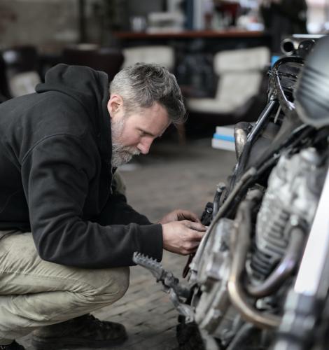 Person in a black sweatshirt and tan pants works on a motorcycle in their garage.