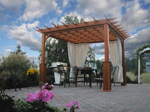 Traditional brown wood pergola with white cloth gathered sides with a dining table and chairs inside.