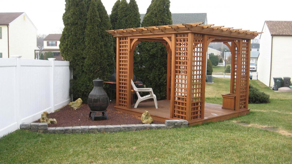 10x10 Wood Traditional Pergola next to a tall white fence and privacy trees.