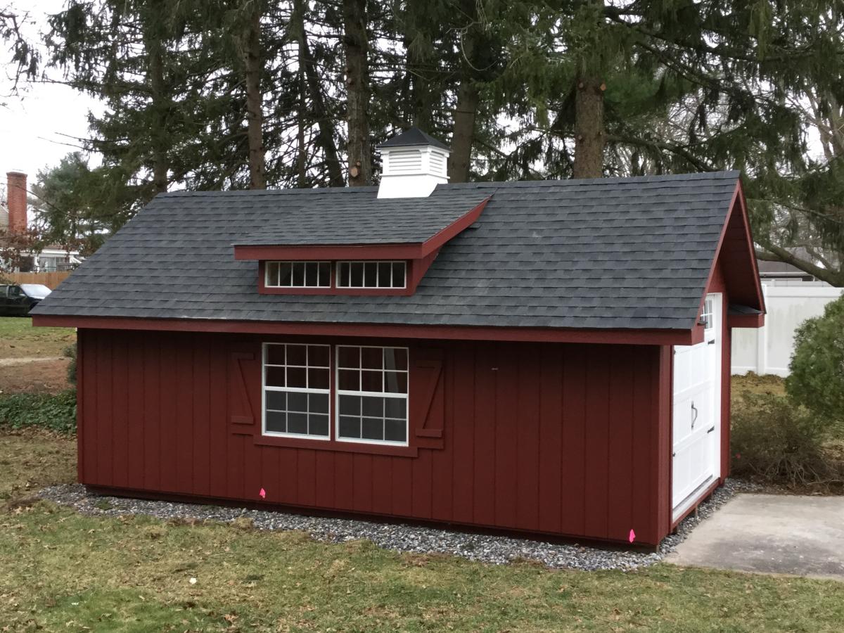 Deluxe Classic Cottage with red siding, windows with red shutters, white double doors, gray roofing, and a white cupola.