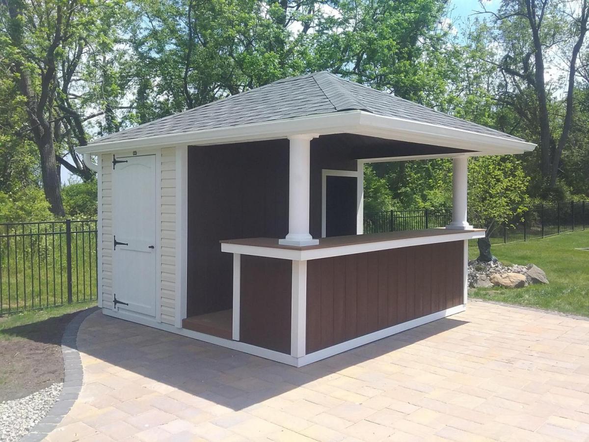 White, beige, and brown Hip Roof wood Cabana with white pillars, a white door, gray asphalt roofing, and a brown counter with white trim.