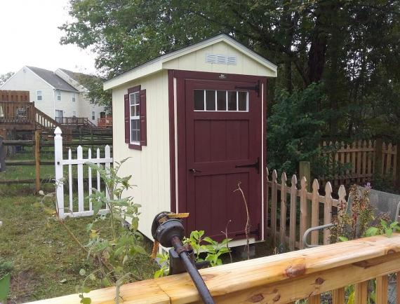 Small custom Garden Shed with white wood siding, red trim, red shutters, and a red door.