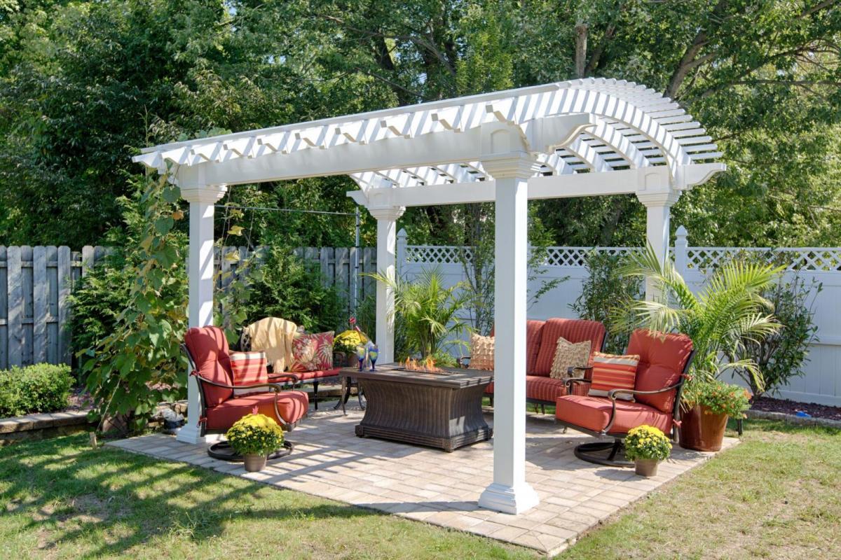 White Vinyl Arcadian Pergola surrounded by vegetation with firepit and chairs underneath.