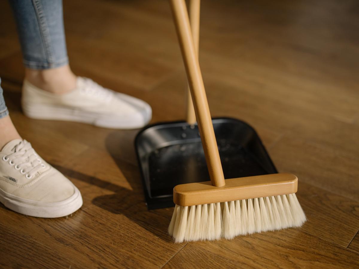Person sweeping wood floor with a broom and free-standing dustpan.