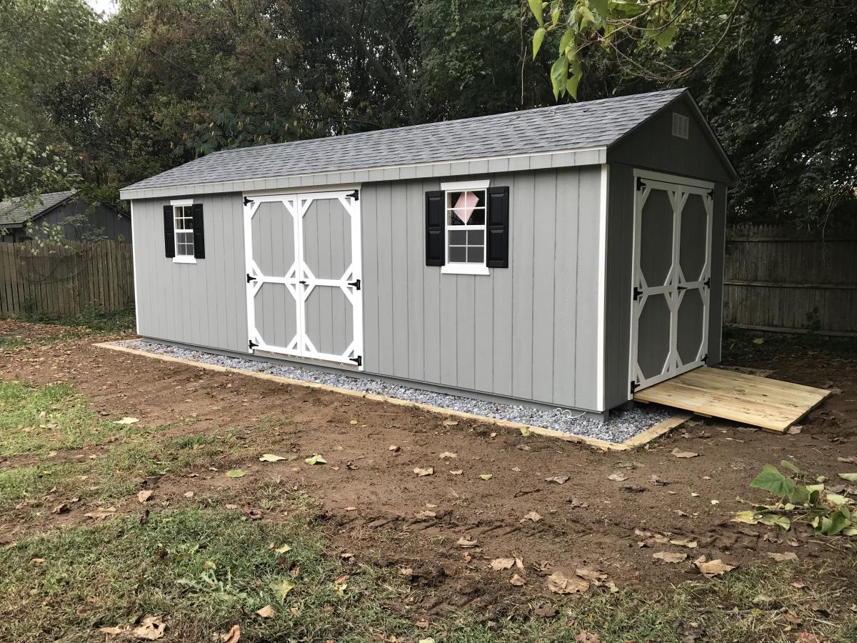 Gray wood storage shed with white trim and black window shutters